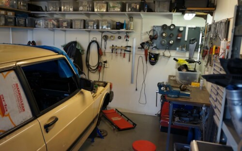 Garage fullt med meckargrejer på väggarna samt en gammal gul bil